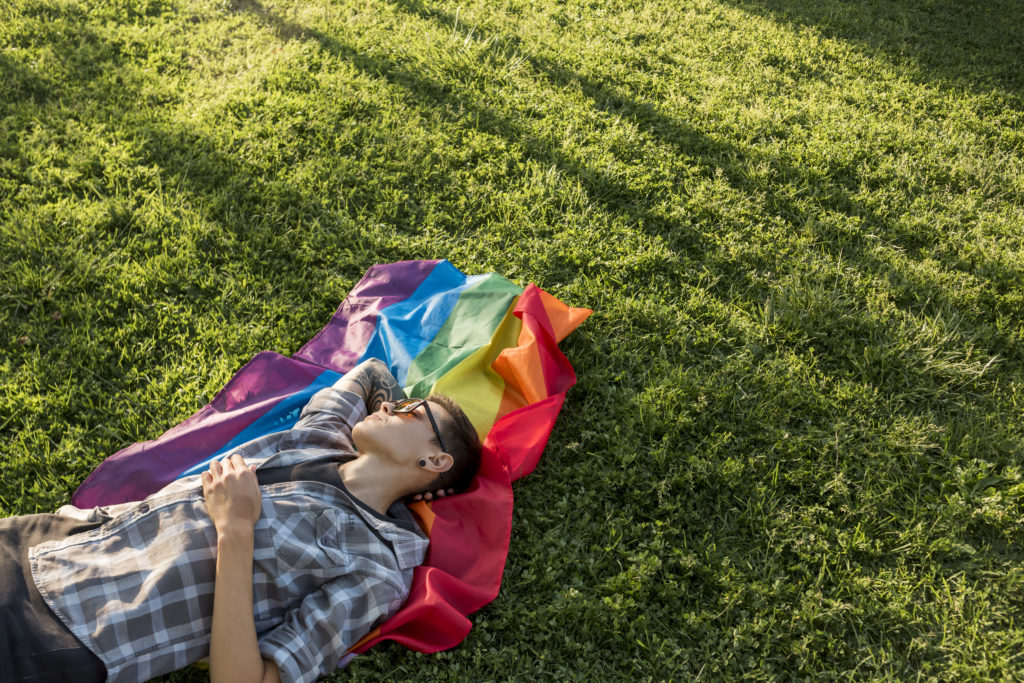 Homme transgenre avec un drapeau LGBT allongé sur une pelouse