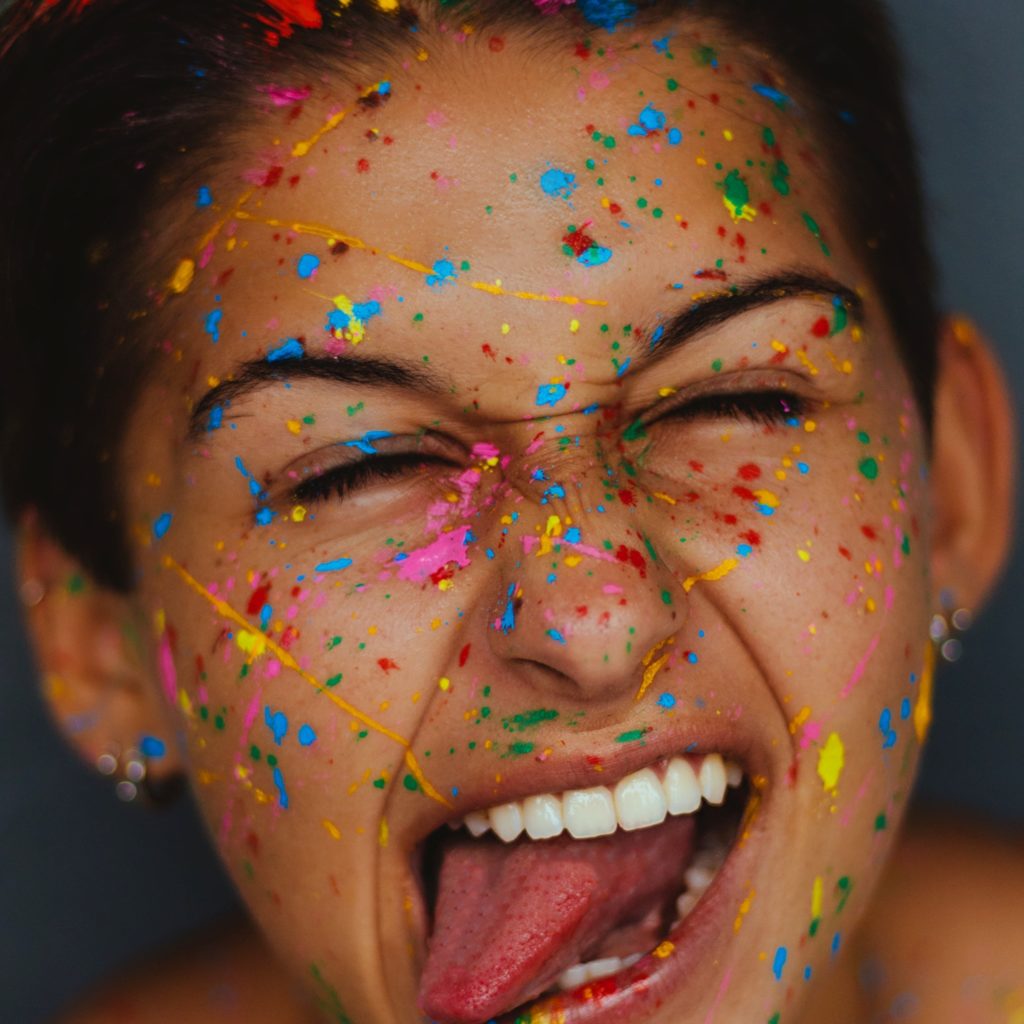 Visage souriant de personne non binaire avec éclaboussures de peinture au couleurs LGBT