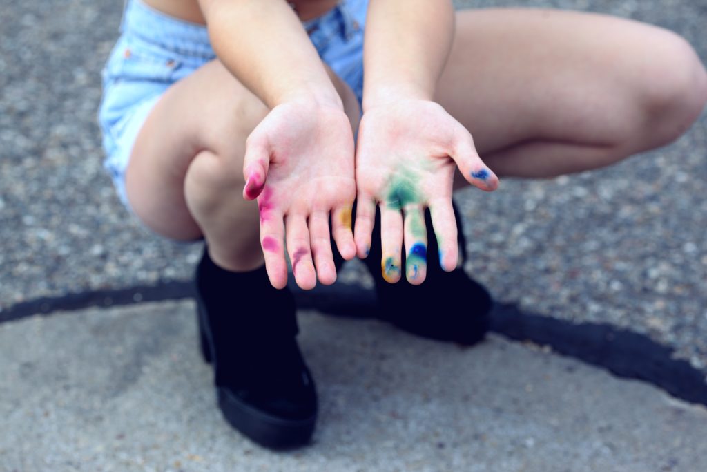 Femme transgenre accroupie montrant ses mains avec des tâches d'encre aux couleurs LGBT